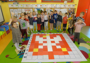 Grupa dzieci stoi wokół maty do kodowania, na której ułożone jest godło Polski z płytek.
